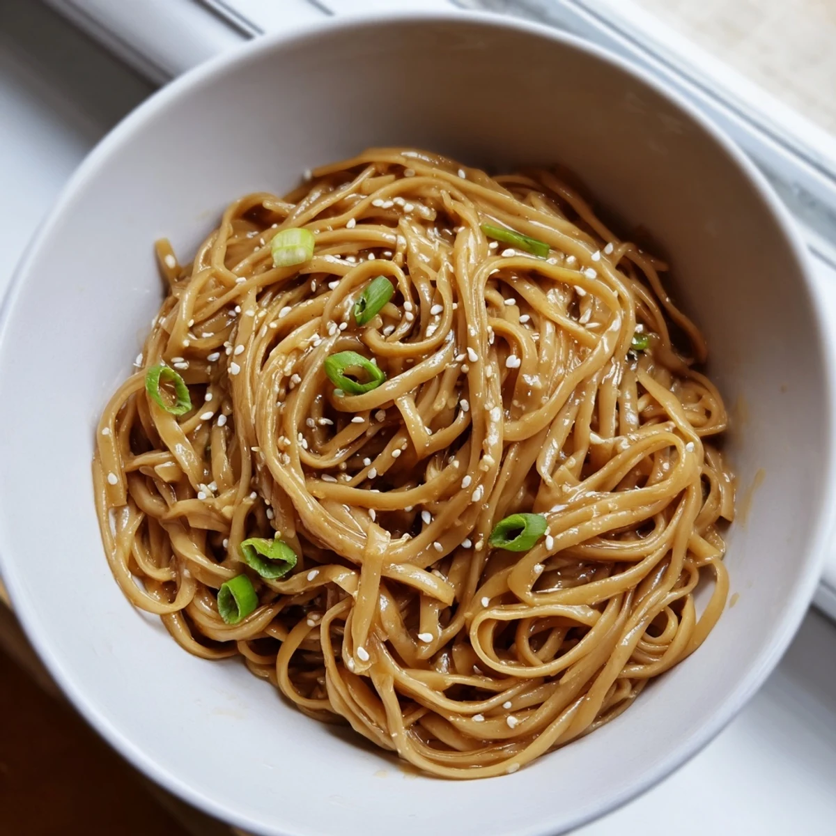 Steaming bowl of Asian Garlic Noodle Bowl featuring tender wheat noodles tossed in rich garlic-butter sauce with red chili slices.  