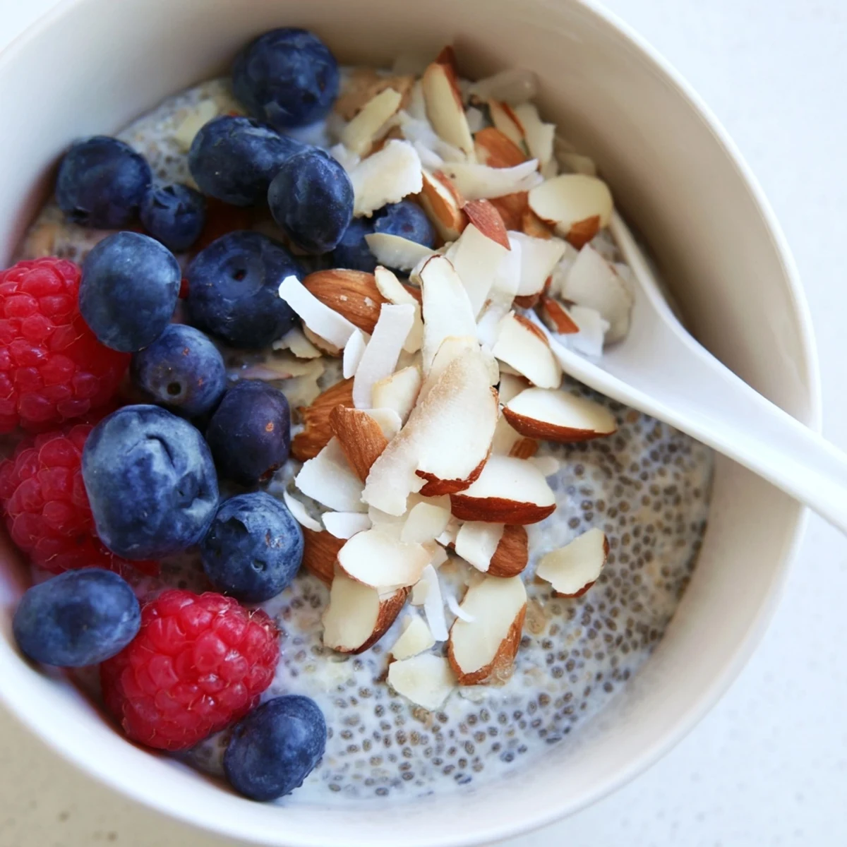 A close-up of poppy seed chia pudding with a sprinkle of toasted almonds and vibrant raspberries, showing its thick, creamy texture.