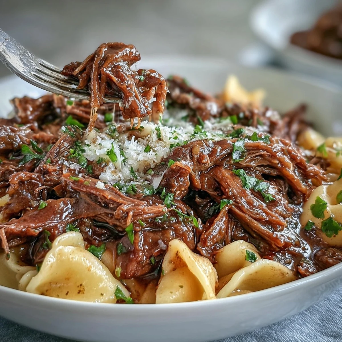 Savory Crockpot French Onion Pot Roast Pasta features shredded beef and caramelized onions over buttery egg noodles, garnished with fresh parsley.
