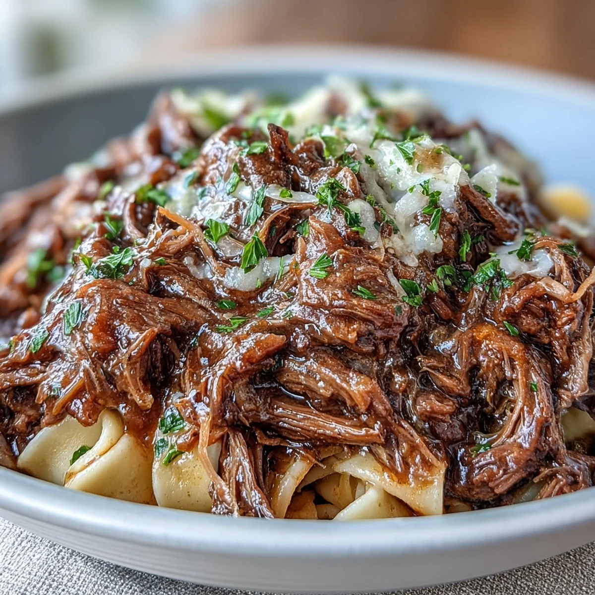 Hearty Crockpot French Onion Pot Roast Pasta twirled on a fork, showcasing tender beef and sweet onions beside buttery noodles on a plate.