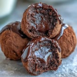 Rich, dark Hojicha Truffles dusted with roasted green tea powder sit on a marble surface, showcasing the creamy ganache texture.