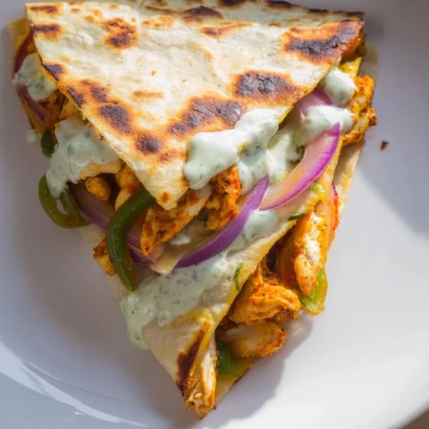 A close-up shot of a delicious Tandoori Chicken Quesadilla, with a creamy yogurt drizzle on top.