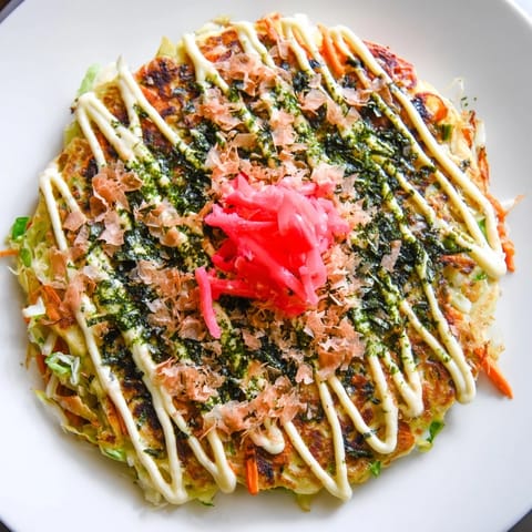 A close-up view of a savory Japanese Okonomiyaki Pancake, loaded with shredded cabbage and garnished with vibrant pickled ginger and aonori.