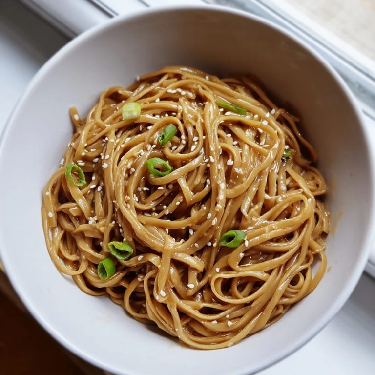 Steaming bowl of Asian Garlic Noodle Bowl featuring tender wheat noodles tossed in rich garlic-butter sauce with red chili slices.  