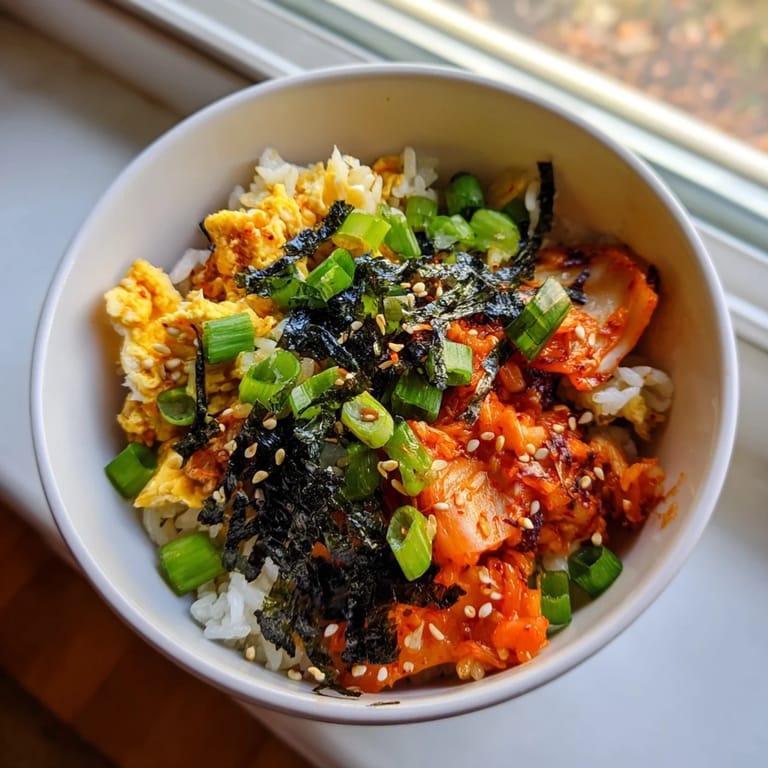 A close-up of Spicy Kimchi Fried Rice topped with a runny egg yolk, sesame seeds, and seaweed.  